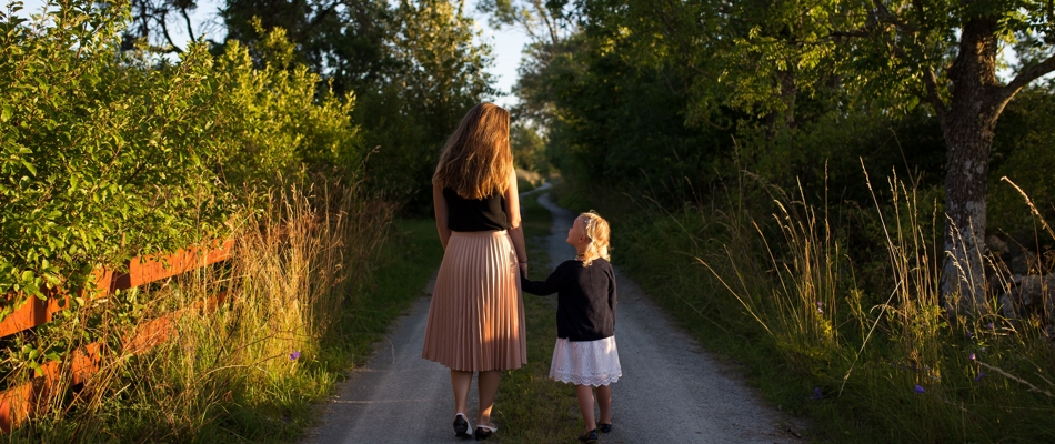 Kvinde går med lille pige i hånden ned af en sti med omkringliggende træer