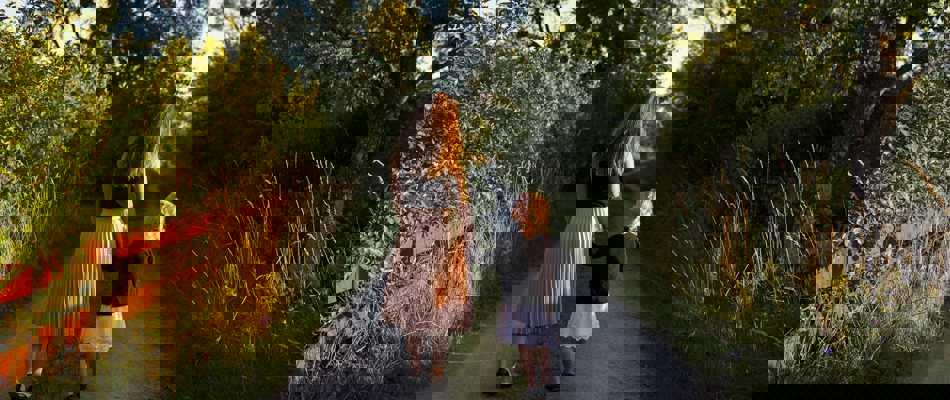 Kvinde går med lille pige i hånden ned af en sti med omkringliggende træer